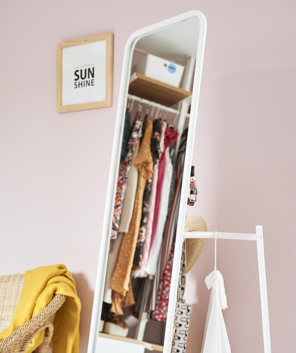 Miroir sur pied avec tringle à l’arrière, à côté d’un mur rose pâle.