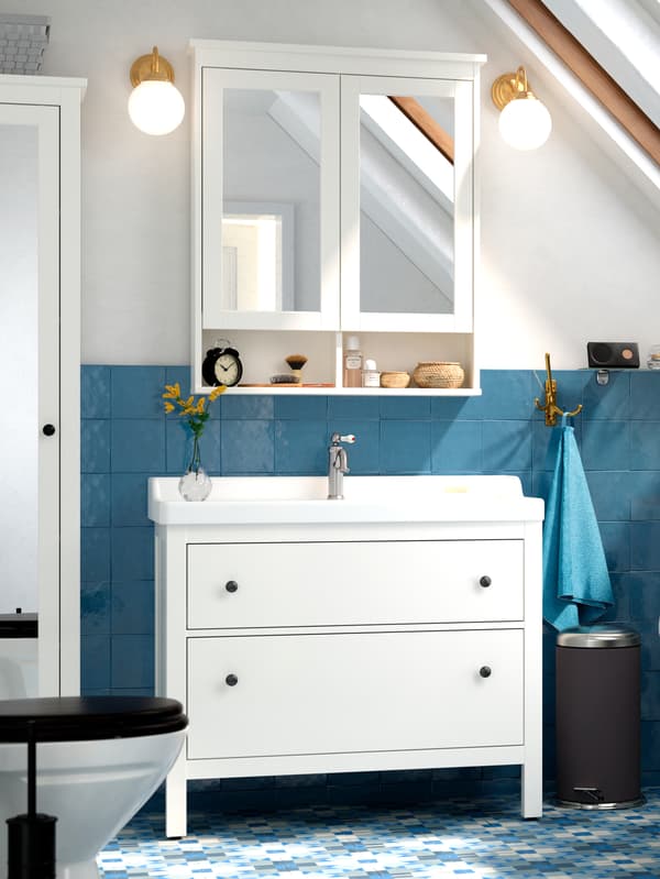 Mirrored HEMNES cupboards above a white wash-basin, with blue wall tiles behind and a blue towel hanging from a hook.