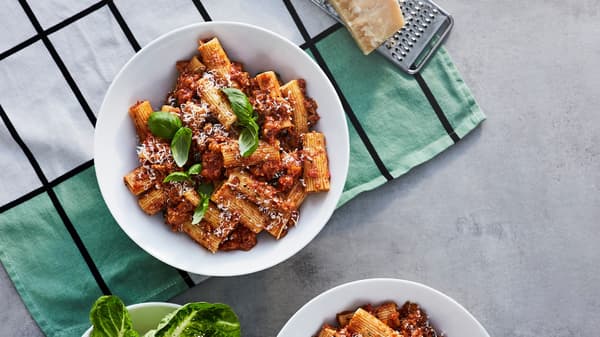 Mísa s boloňskými těstovinami z rostlinného mletého masa VÄRLDSKLOK, s čerstvou bazalkou a strouhaným parmezánem, na kuchyňské utěrce.