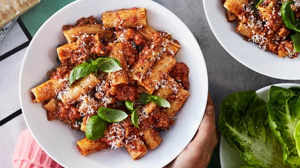 Mísa s boloňskými těstovinami z rostlinného mletého masa VÄRLDSKLOK, s čerstvou bazalkou a strouhaným parmezánem, na kuchyňské utěrce.