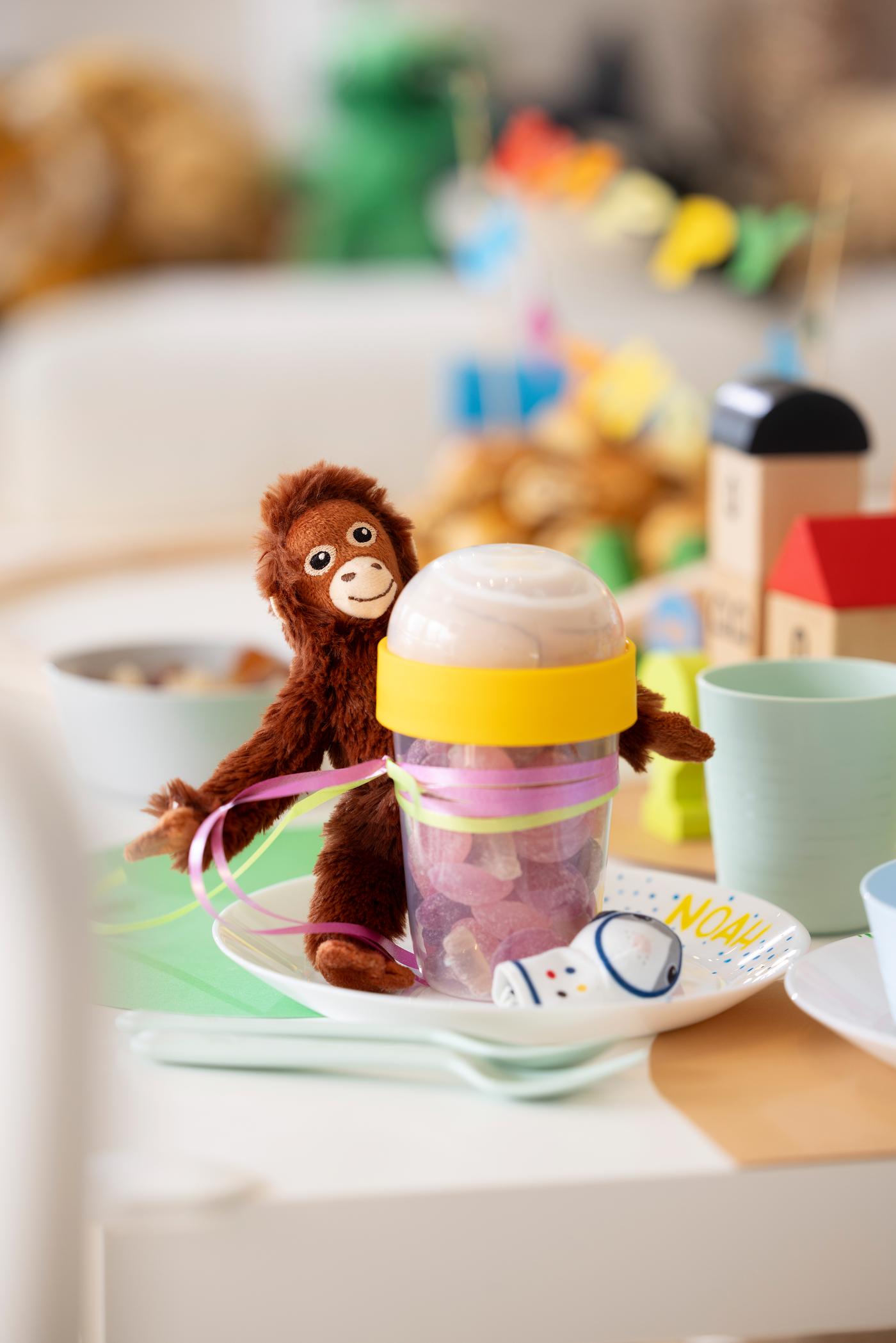 Mitgebsel auf einem Teller. Zu sehen ist eine kleine SNackbox gefüllt mit Süßigkeiten und einem Affenkuscheltier daran gebunden. 