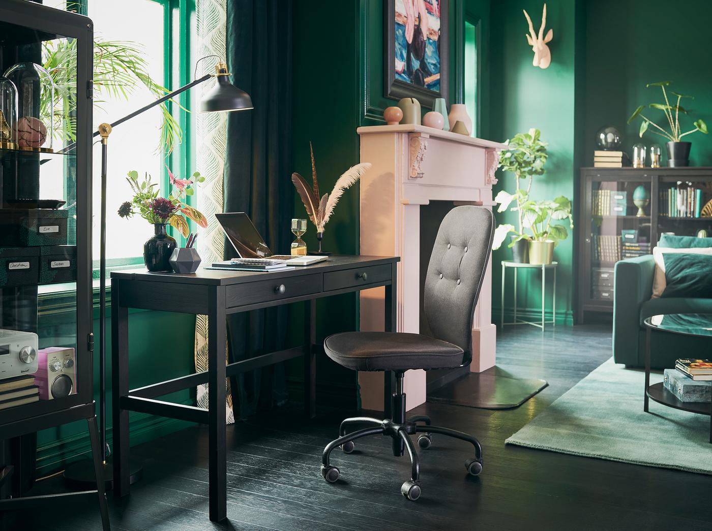 مكتب أسود بني بجوار النافذة في غرفة جلوس ذات جدران خضراء ومدفأة وردي.