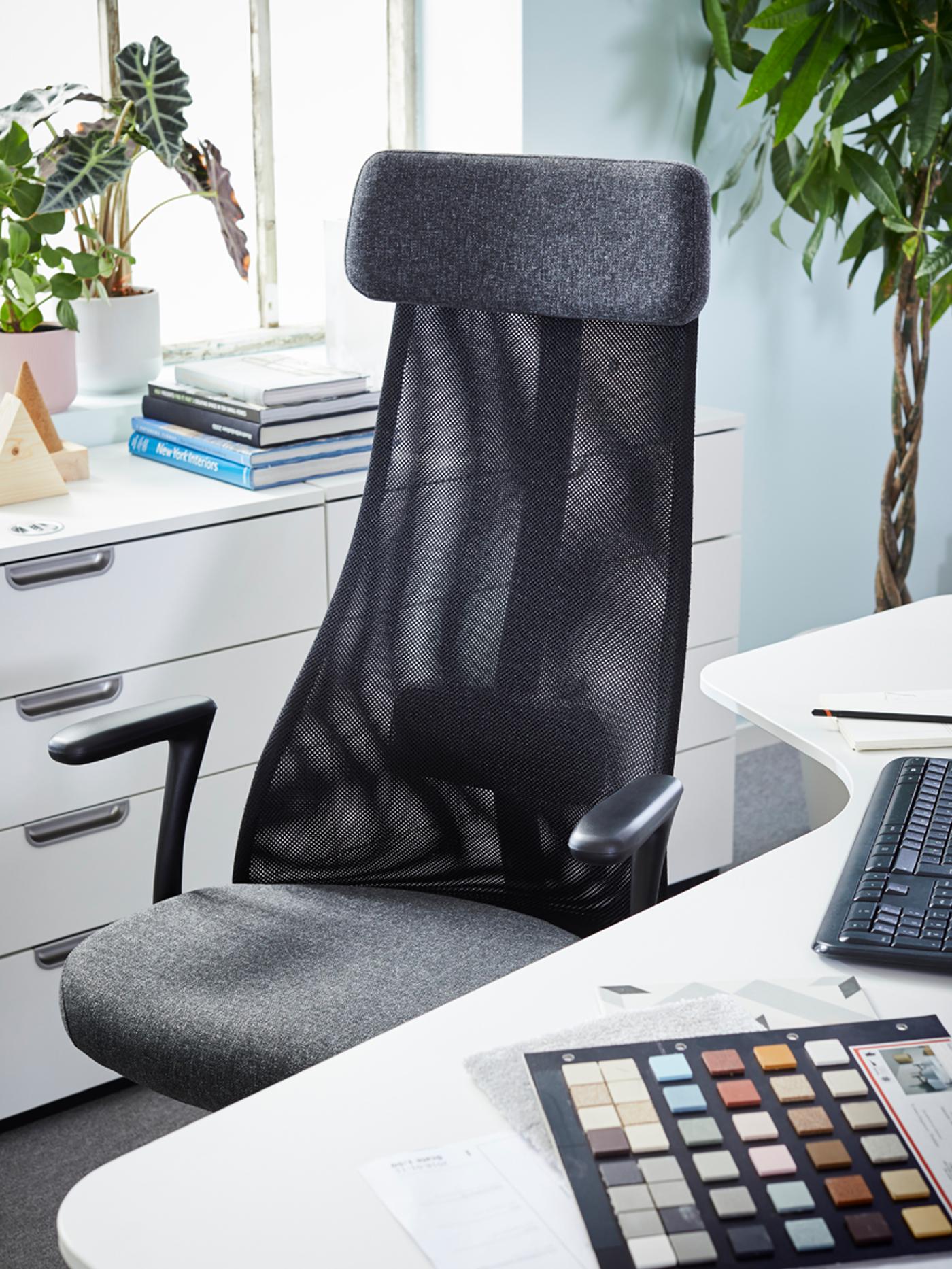 مكتب زاوية BEKANT وكرسي مكتبي JÄRVFJÄLLET باللون الرمادي الداكن بجانب نافذة بها آنية نباتات وكومة من الكتب.