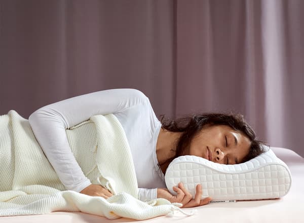 Mladá žena ležící na boku zdravě spí na ergonomickém polštáři ROSENSKÄRM