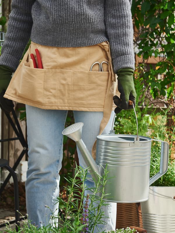 Mladá žena v pracovní zástěře drží v ruce konev KORKGRAN.