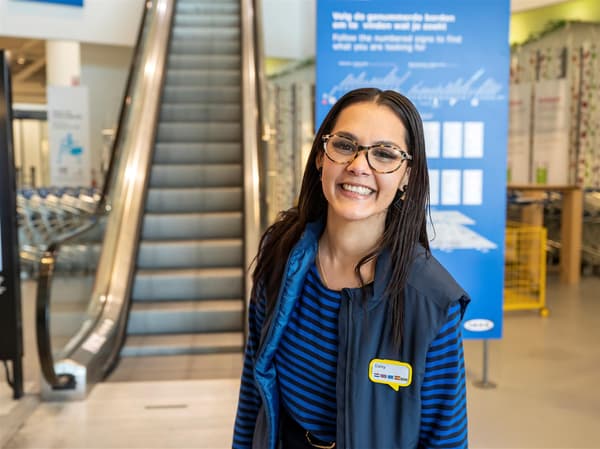 Mladá žena v uniforme IKEA pózuje s úsmevom v priestoroch obchodného domu IKEA.