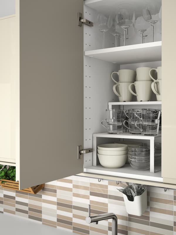 Mobile per cucina con anta beige chiaro lucido aperta per mostrare articoli per la tavola riposti su ripiani all’interno - IKEA