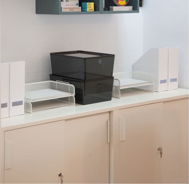 Moble d’oficina amb caixes i safates organitzadores sobre una superfície blanca, al costat d’arxivadors verticals.