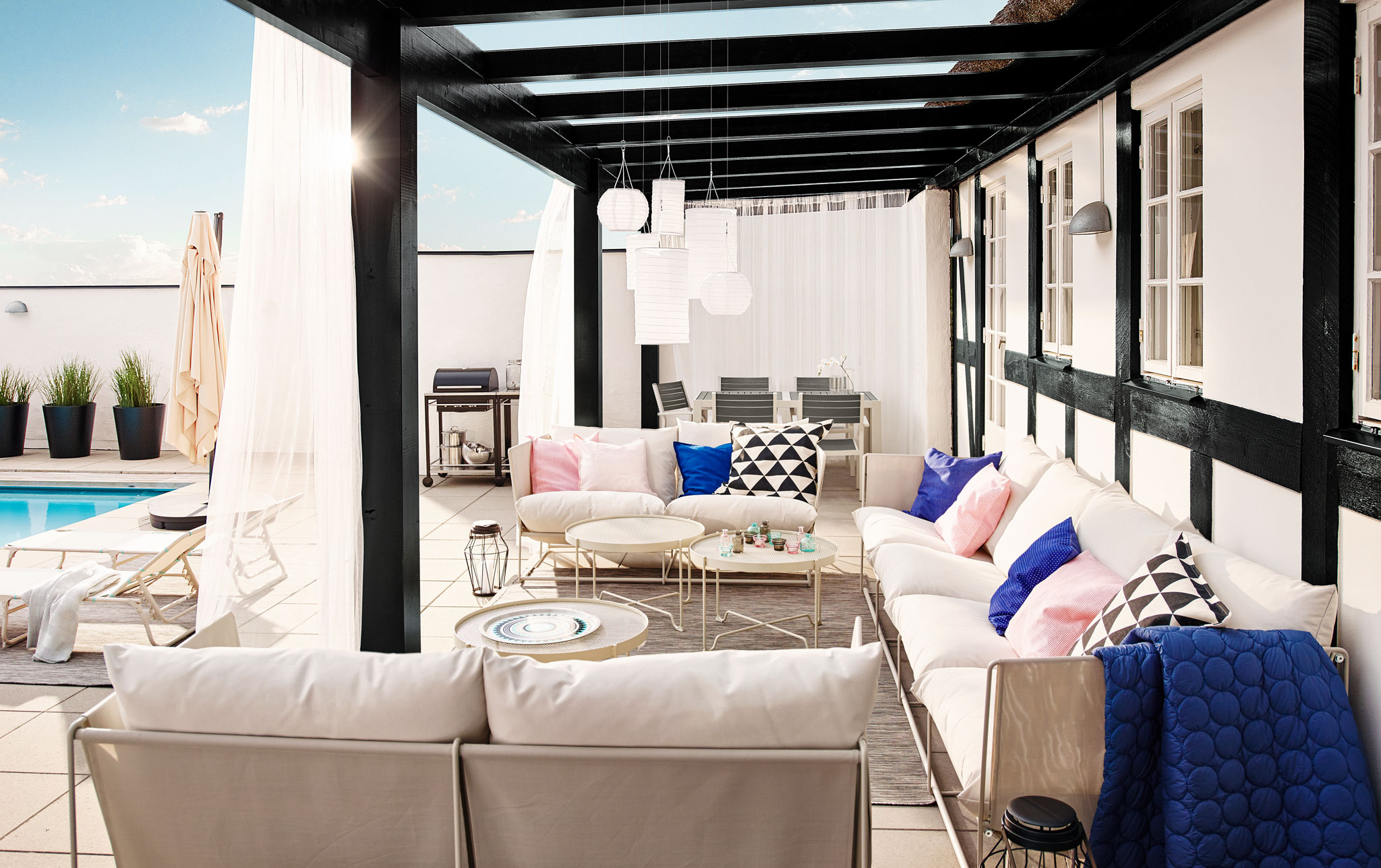 Modern and durable four-seat and two-seat in/outdoor HAVSTEN sofa in beige, under a covered terrace in a garden with a pool.