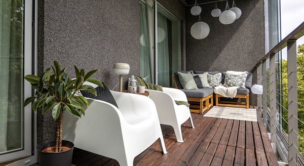 Modern balcony with white chairs, potted plant and cozy seating area.