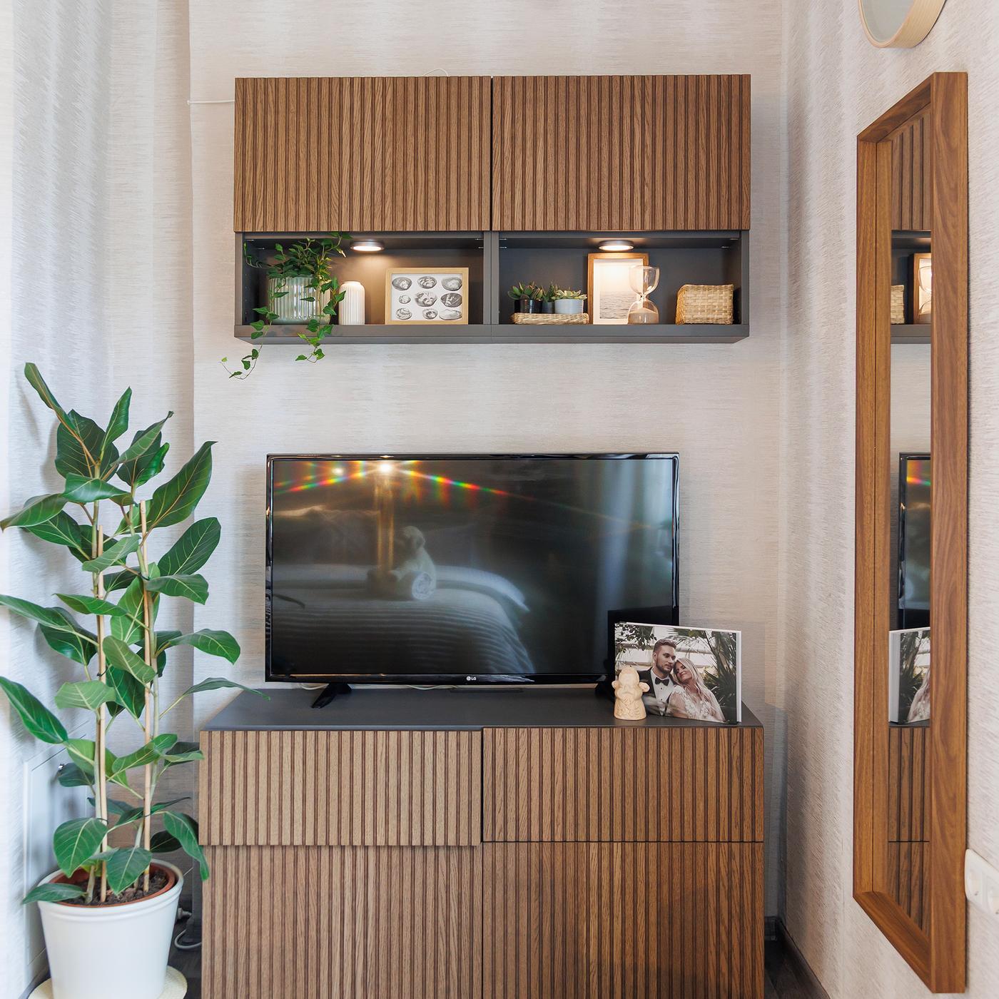 Modern bedroom corner with a wooden TV bench and wall cabinets, decorated with plants and books.