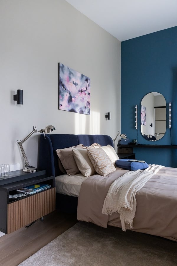 Modern bedroom corner with blue accent wall, artwork above bed, and vanity mirror