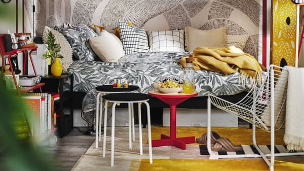 Modern bedroom with patterned bedding, colorful tables, yellow throw blanket, and graphic wall mural.