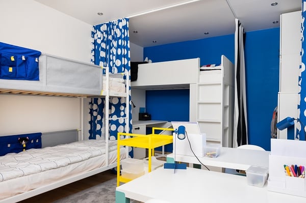 Modern children’s room with bunk beds, study desks, blue walls, and storage