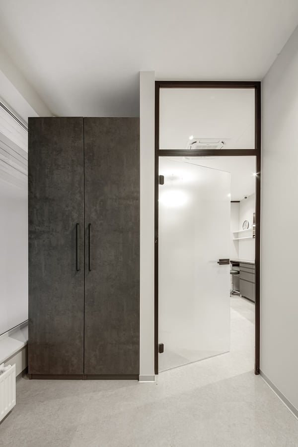 Modern dental clinic entrance to treatment room with frosted glass door and tall dark storage cabinet.