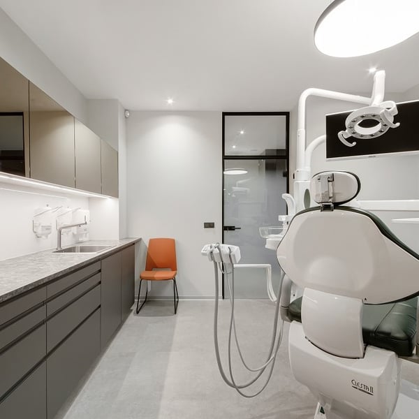 Modern dental clinic interior with green dentist chair, overhead light, and sleek cabinets, featuring an orange chair in the corner.