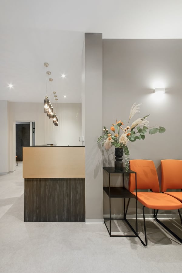 Modern dental clinic waiting area with orange chairs, decorative flower arrangement, and stylish pendant lighting at the reception desk.