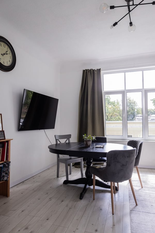 Modern dining area with round table, upholstered chairs, wall-mounted TV, and natural light