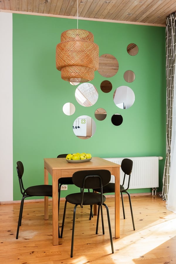 Modern dining area with wooden table, black chairs, green accent wall, and decorative mirrors