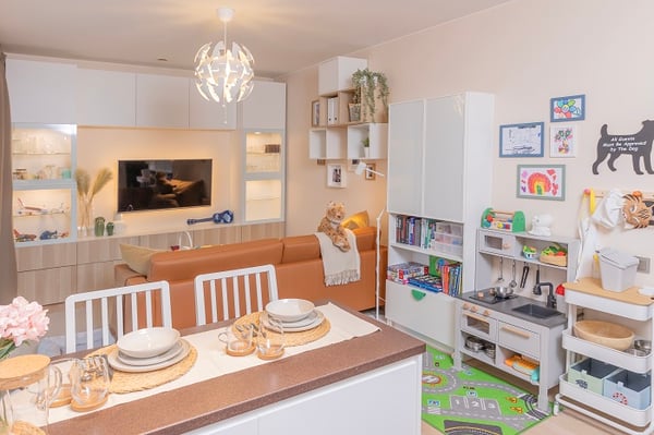 Modern family living space with kitchen, sofa, and kids’ corner.