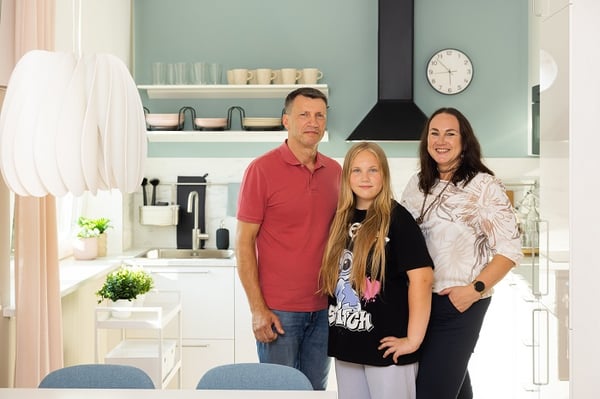 Modern family standing in a bright, stylish kitchen with white cabinets and pastel blue walls
