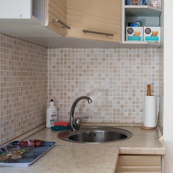 Modern kitchen sink area with mosaic tile backsplash and light wood cabinets