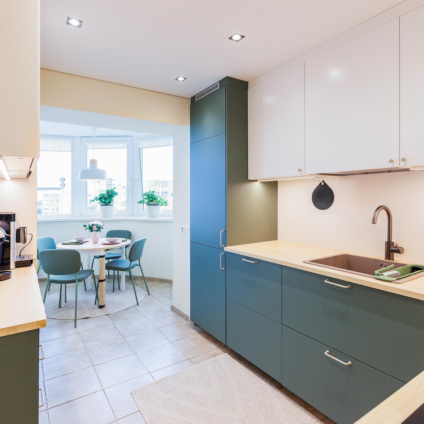 Modern kitchen with green lower cabinets and white upper cabinets, wooden countertops, built-in appliances and a small dining area by a window.