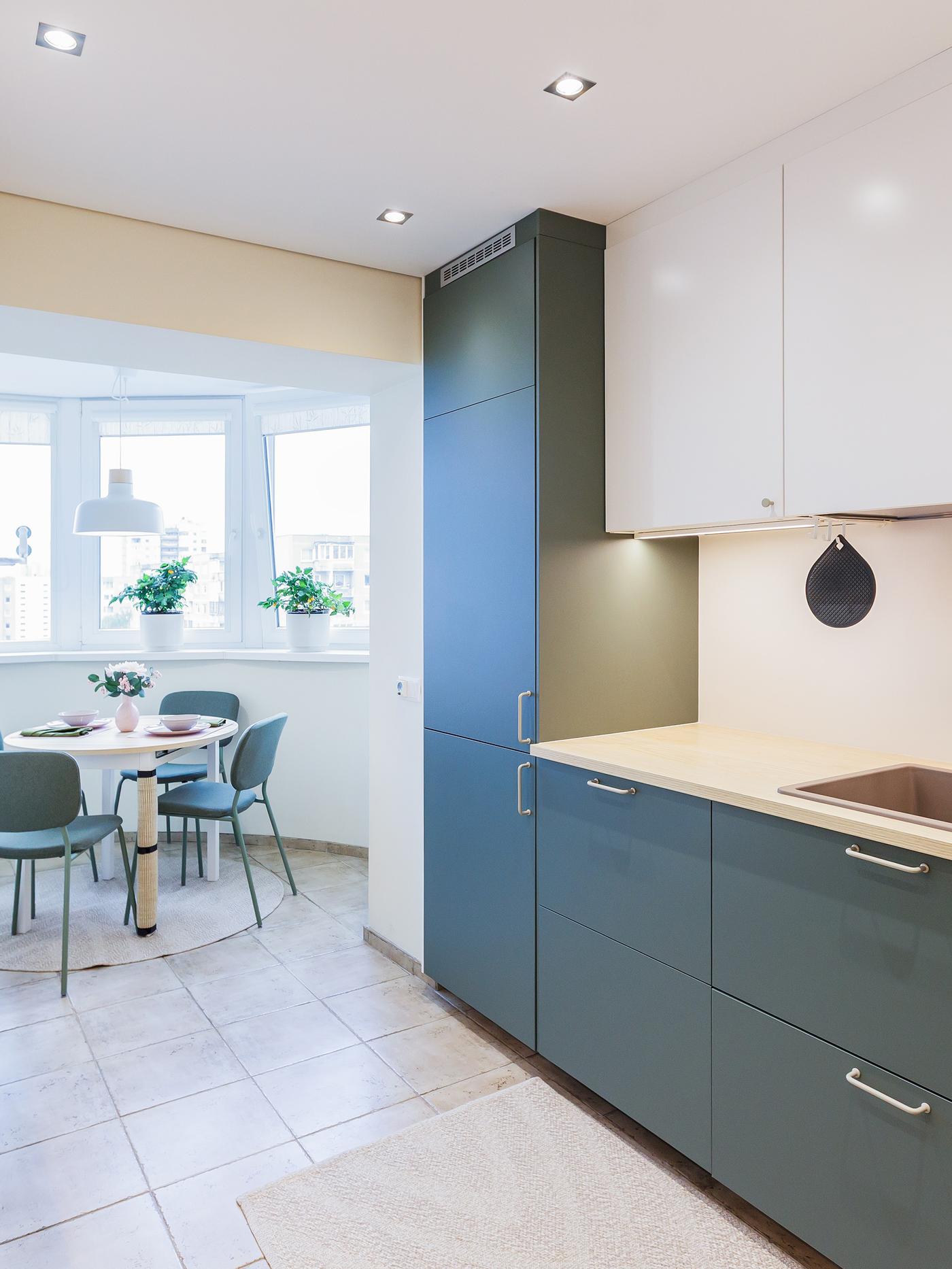 Modern kitchen with green lower cabinets and white upper cabinets, wooden countertops, built-in appliances and a small dining area by a window.