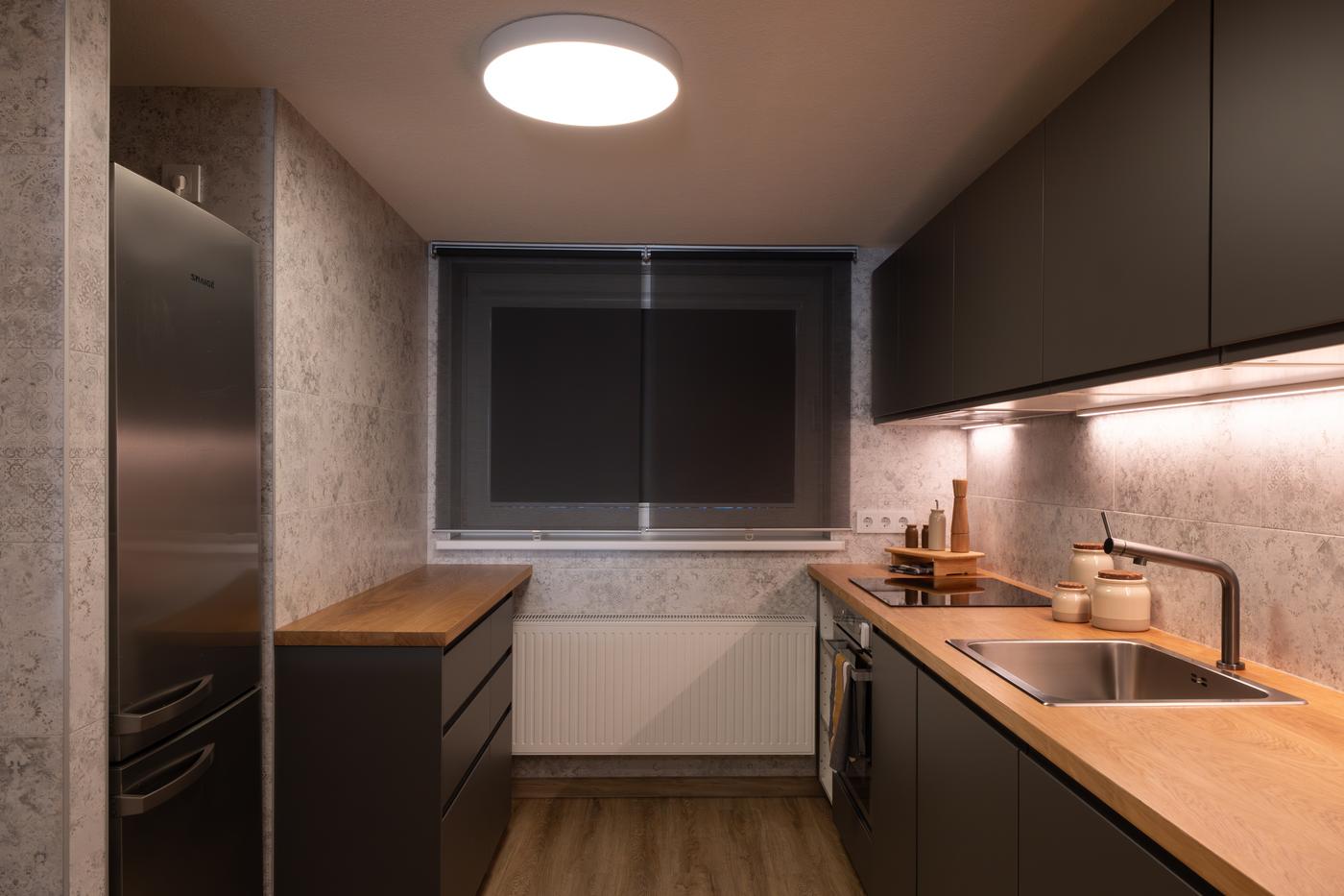 Modern kitchen with warm wooden worktops, dark fronts, and under-cabinet lighting.