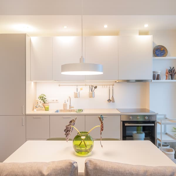 Modern kitchen with white cabinets, dining table, and green decor vase.