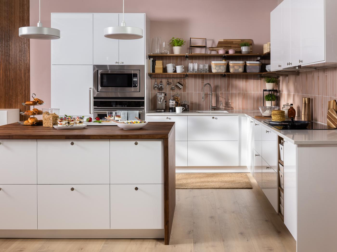 Modern kitchen with white cabinets, wooden countertops, open shelves with dishes, and pendant lights. Food and snacks are arranged on the island countertop.
