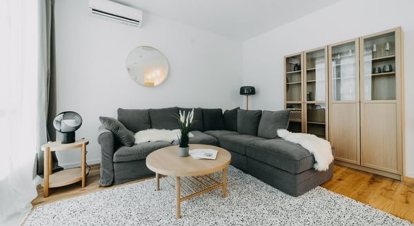 Modern living room with dark grey sectional sofa, round wooden coffee table, and glass-door wooden cabinets.