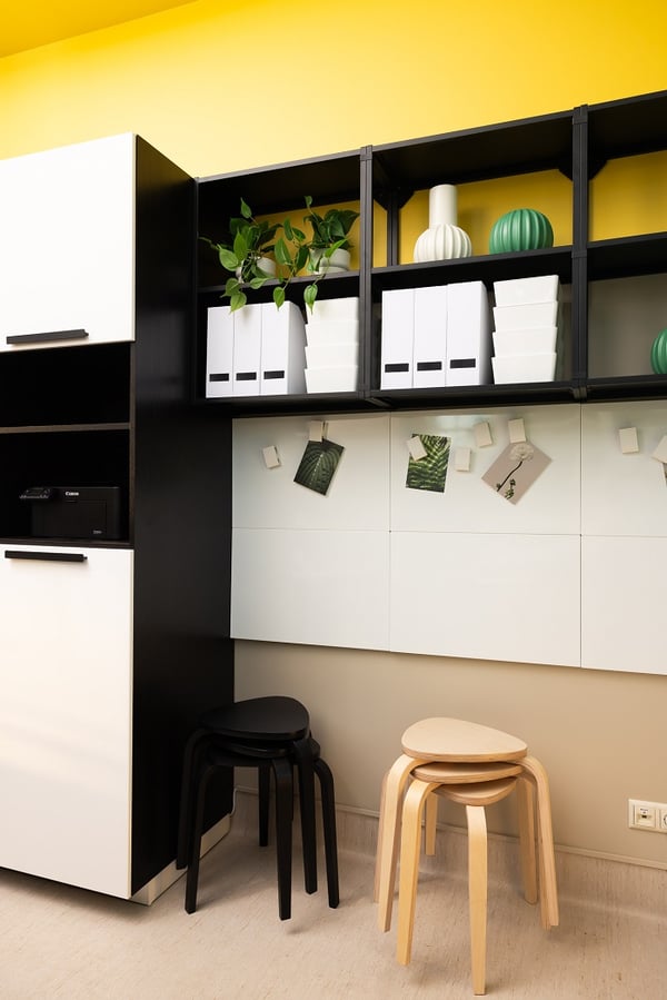 Modern office storage area with black shelving, white cabinets and yellow accent wall