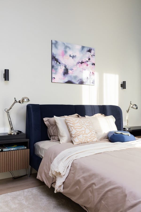 Modern upholstered bed with neutral bedding, bedside lamps, and abstract wall art