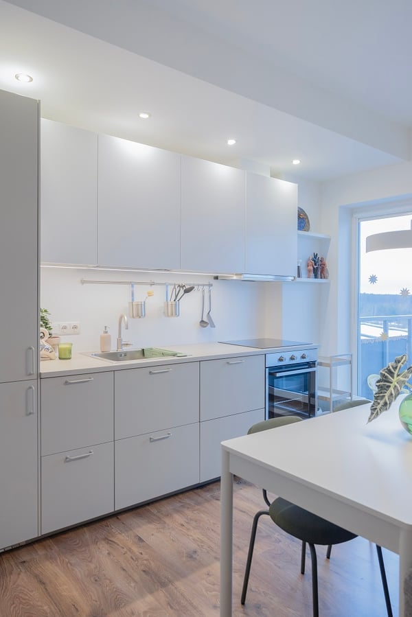 Modern white kitchen with built-in oven, sink, and dining table.