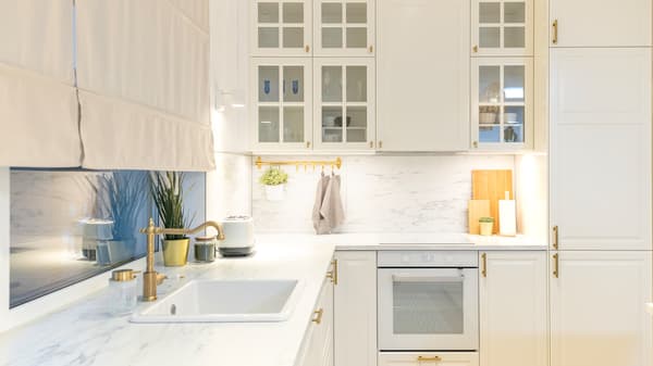 Modern white kitchen with marble countertop, gold handles, and built-in oven.