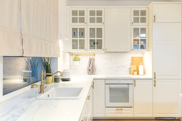 Modern white kitchen with marble countertop, gold handles, and built-in oven.