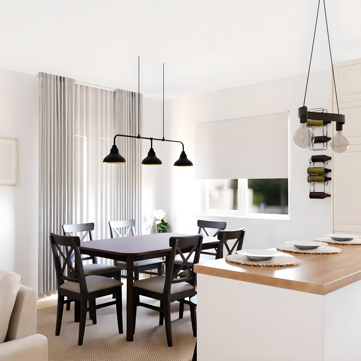 Moderna blagovaonica s drvenim stolom, šest crnih stolica, tri viseće lampe, bijelim zavjesama na prozorima te kuhinjskim otokom s drvenom pločom i tanjurima na podmetačima.