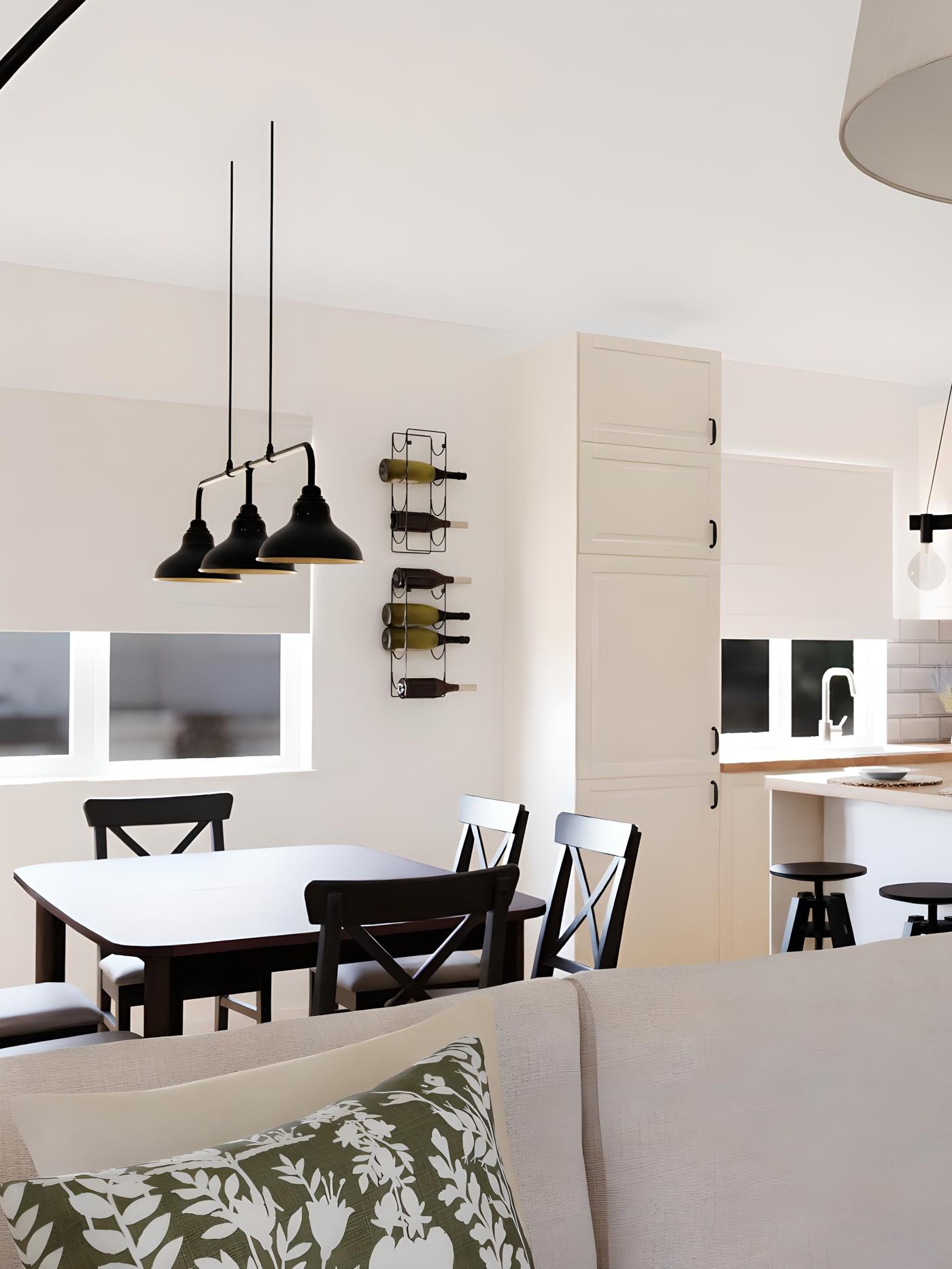 Moderna kuhinja s bijelim ormarićima, drvenim stolom, crnim stolicama, policama s vinima, tri crne viseće lampe te kuhinjskim otokom s barskim stolicama i sudoperom ispod prozora.