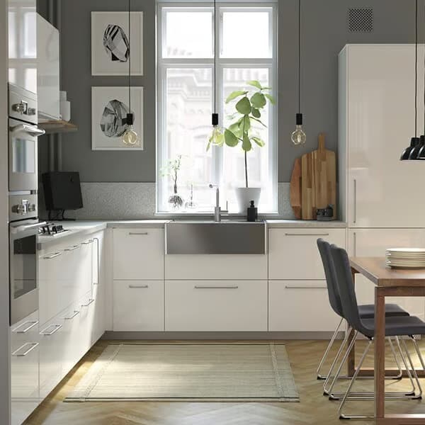 Modernes IKEA Küchendesign mit weißen Hochglanzfronten und dunklen Wandakzenten. Große Fenster lassen viel Tageslicht herein. Hängende Lampen, ein Holz-Esstisch und stilvolle Küchenaccessoires ergänzen das minimalistische Konzept.