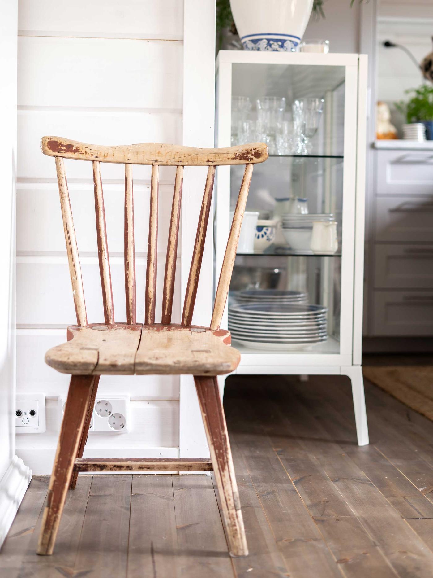 Modernissa mökissä on puinen, perinteistyylinen tuoli ja valkoinen vitriinikaappi.