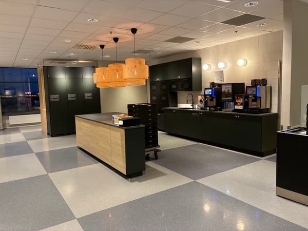 Modernt kök- och kaffehörna i IKEA Malmös personalmatsal med mörka skåp, flera kaffemaskiner, köksö och hänglampor i rotting.