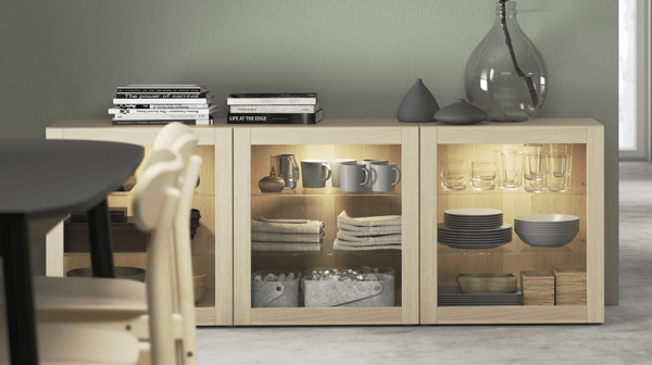 Mòdul baix amb vitrines de fusta clara il·luminades, decorat amb vaixella i tèxtils organitzats, ideal per a sales d’estar o menjadors amb estil acollidor.
