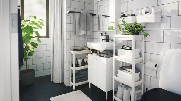 Monochromatic contemporary styled bathroom with several space saving storage units, trolley and indoor green plants.