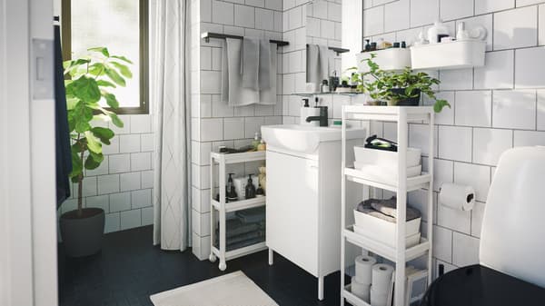 Monochromatic contemporary styled bathroom with several space saving storage units and boxes and indoor green plants.