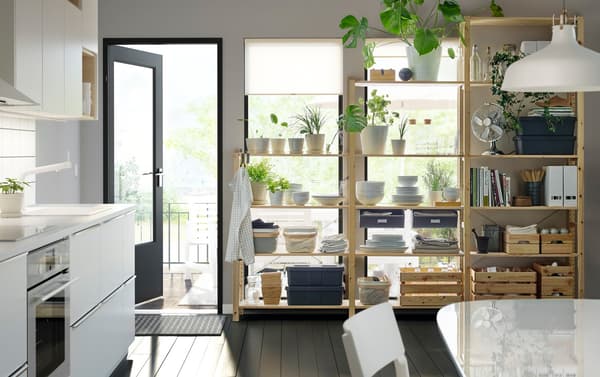 Monochrome keuken met planten, eetgerei en dozen op IVAR houten planken. De deur naar de tuin staat open.