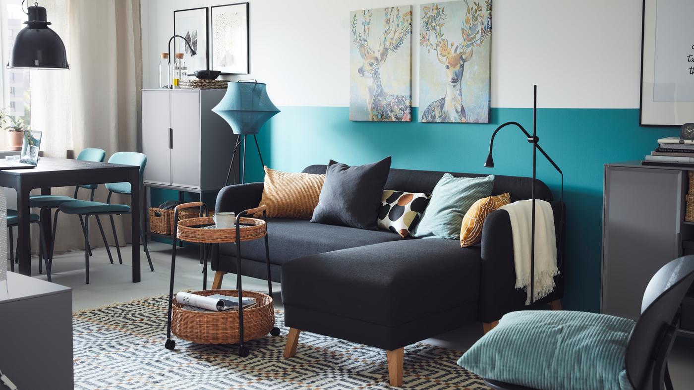 Mørkegrå LINANÄS sofa med sjeselong bak et trillebord av rotting i ei solrik stue i blå og grå fargetoner.