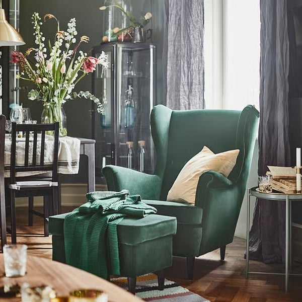 Mørkegrøn STRANDMON stol står i en stue hvor der også ses andre møbler. Lyset falder ind gennem vinduet og der står en stor blomster på spisebordet