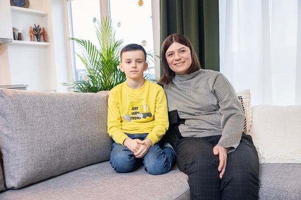 Mother and son sitting together on a grey sofa in modern living room.