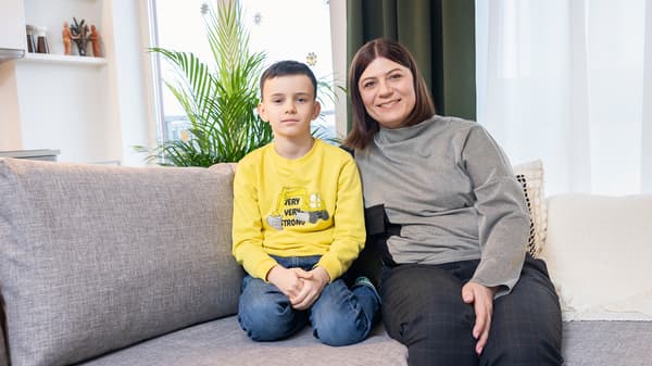 Mother and son sitting together on a grey sofa in modern living room.